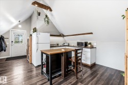 Angled ceilings with exposed wood beams, wood-finish flooring, white cabinetry, dark countertops, and a white paneled door with glass inserts - 