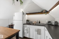 Kitchenette with vaulted ceilings, white cabinetry, dark countertops, and a stainless steel sink - 