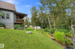 Expansive backyard featuring a covered deck, vibrant garden beds, and mature trees - 