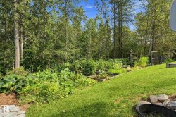 Expansive backyard featuring a manicured lawn, raised garden beds, and mature trees - 