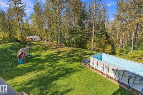 Expansive backyard featuring mature pine and evergreen trees, manicured lawn, and a saltwater pool with integrated lounging ledge - #45 53122 Rge Road 14, Rural Parkland County, AB 