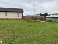 Expansive green lawn with a wood fence, featuring a garden bed and a greenhouse structure - 