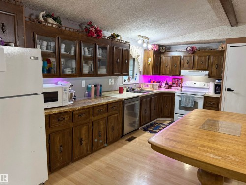Kitchen featuring wood-finish cabinetry, light countertops, wood-finish flooring, white appliances, and a built-in kitchen sink - 4626 51 Avenue, Willingdon, AB 