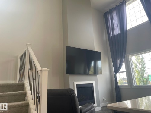 Two-story windows, vaulted ceiling, white trim fireplace, carpeted stairs, and white and black wrought iron railing - 7939 Erasmus Crescent Nw, Edmonton, AB 