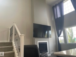 Two-story windows, vaulted ceiling, white trim fireplace, carpeted stairs, and white and black wrought iron railing - 