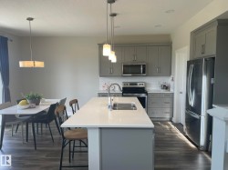 Kitchen featuring an island with an undermount sink, gray cabinetry, stainless steel appliances, and wood-finish flooring - 