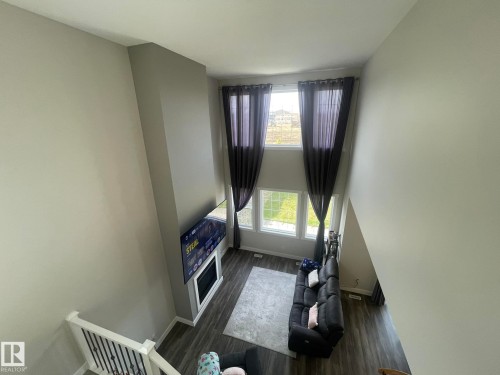 Two-story living area with high ceilings, multiple windows, built-in fireplace, and wood-finish flooring - 7939 Erasmus Crescent Nw, Edmonton, AB 