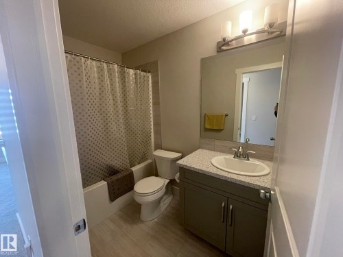 Bathroom featuring a vanity with an integrated sink, a speckled countertop, and a built-in mirror with overhead lighting - 7939 Erasmus Crescent Nw, Edmonton, AB 