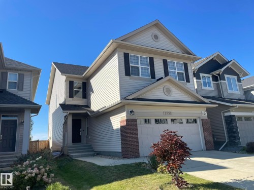 Two-story residence featuring light-colored siding, dark shutters, an attached garage, and a covered entry - 7939 Erasmus Crescent Nw, Edmonton, AB 