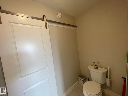 White paneled barn door with a stainless steel track, light-toned wall paint, and a white toilet - 7939 Erasmus Crescent Nw, Edmonton, AB 