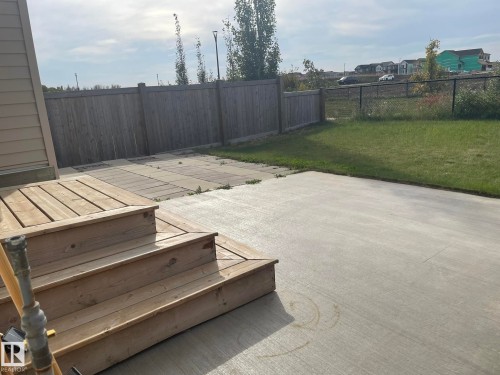 Wood deck with steps leading to a concrete patio, bordered by a wood privacy fence and a chain-link fence, featuring a grass area - 7939 Erasmus Crescent Nw, Edmonton, AB 