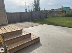 Wood deck with steps leading to a concrete patio, bordered by a wood privacy fence and a chain-link fence, featuring a grass area - 