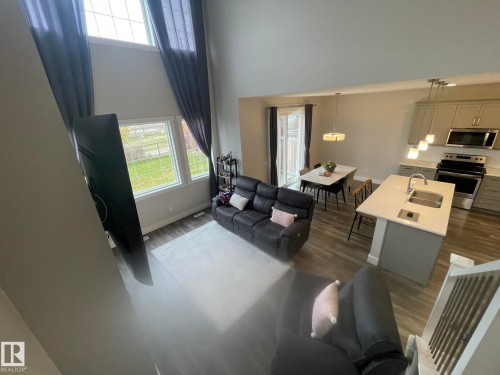 Double-height ceiling, large windows, wood-finish flooring, central kitchen island with integrated sink, and stainless steel appliances - 7939 Erasmus Crescent Nw, Edmonton, AB 