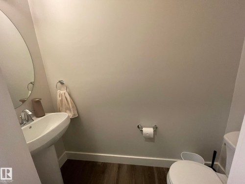 Pedestal sink with chrome faucet, oval mirror, wood-finish flooring, and white baseboards - 7939 Erasmus Crescent Nw, Edmonton, AB 