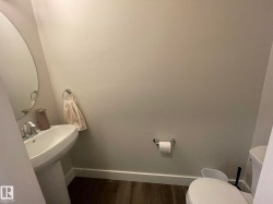Pedestal sink with chrome faucet, oval mirror, wood-finish flooring, and white baseboards - 