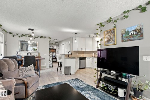 Open-concept living space featuring wood-finish flooring, a kitchen with white cabinetry and stainless steel appliances, and a dining area with pendant lighting - 38 Red Tail Way, St. Albert, AB 