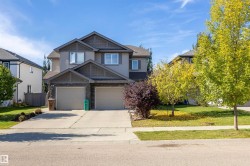 Two-story dwelling with a concrete driveway, dual garage doors, and a stone facade accent - 