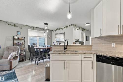 Kitchen featuring white cabinetry, granite-style countertops, stainless steel dishwasher, and a tile backsplash - 38 Red Tail Way, St. Albert, AB 