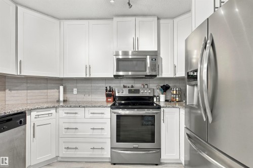 White shaker-style cabinetry with brushed nickel hardware, stainless steel appliances, speckled countertops, and a subway tile backsplash - 38 Red Tail Way, St. Albert, AB 