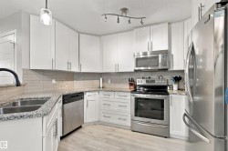 White cabinetry, stainless steel appliances, granite countertops, tile backsplash, and wood-finish flooring - 
