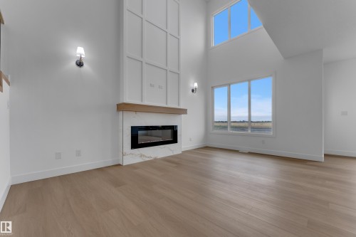 Two-story fireplace with a custom wood mantle, integrated linear electric fireplace, and marble-finish surround - 794 Bank Drive, Leduc, AB 