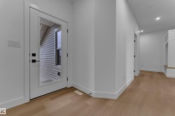 Light wood-finish flooring, recessed lighting, white walls, built-in storage bench, and a white door with a clear glass panel - 