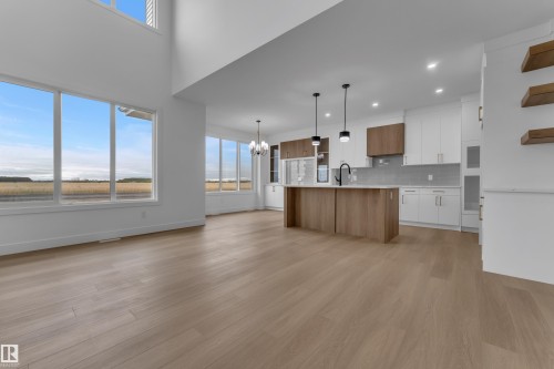 Expansive open-concept living area featuring high ceilings, wood-finish flooring, a modern kitchen island with pendant lighting, and abundant natural light through large windows - 794 Bank Drive, Leduc, AB 