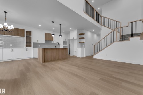 Open-concept living area featuring wood-finish flooring, a contemporary kitchen with white and wood-tone cabinetry, a central island, and a staircase with open risers and metal balusters - 794 Bank Drive, Leduc, AB 