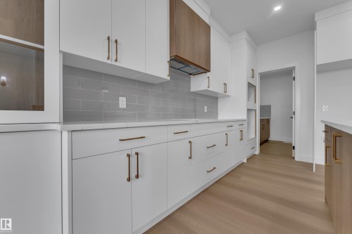 White cabinetry with gold-toned hardware, light gray subway tile backsplash, white countertops, wood-finish flooring, and a wood-paneled range hood - 794 Bank Drive, Leduc, AB 