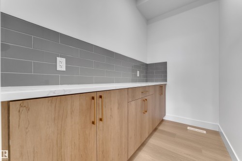 Wood-finish cabinetry with golden hardware, white countertop, grey subway tile backsplash, and wood-finish flooring - 794 Bank Drive, Leduc, AB 