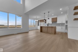 Expansive open-concept living area featuring high ceilings, wood-finish flooring, a modern kitchen island with pendant lighting, and abundant natural light through large windows - 
