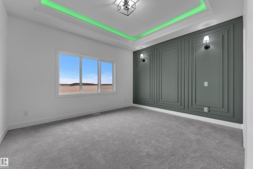 Tray ceiling with integrated lighting, wall paneling, sconce lighting, wide window, and grey carpeting - 794 Bank Drive, Leduc, AB 