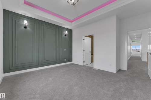 Tray ceiling with accent lighting, decorative wall paneling, wall-mounted sconces, plush grey carpeting, and white baseboards - 794 Bank Drive, Leduc, AB 