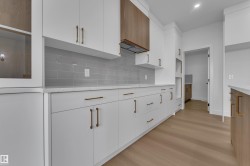 White cabinetry with gold-toned hardware, light gray subway tile backsplash, white countertops, wood-finish flooring, and a wood-paneled range hood - 