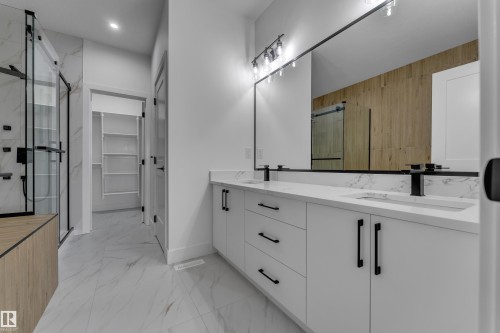 Bathroom featuring a dual vanity with white cabinetry, integrated sinks, and black fixtures - 794 Bank Drive, Leduc, AB 