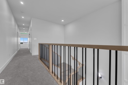 Open hallway with recessed lighting, light-toned wood-finish handrail, black balusters, and grey carpet flooring - 794 Bank Drive, Leduc, AB 