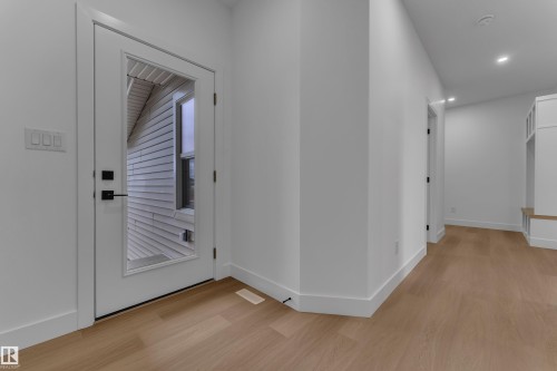 Light wood-finish flooring, recessed lighting, white walls, built-in storage bench, and a white door with a clear glass panel - 794 Bank Drive, Leduc, AB 