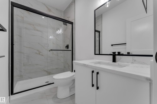 Sleek bathroom featuring a tiled shower with a black-framed glass enclosure, a white toilet, and a vanity with a white countertop and integrated sink - 794 Bank Drive, Leduc, AB 