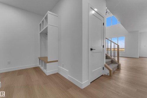 Built-in storage bench with cubbies, light wood-finish flooring, white solid core door with matte black hardware, carpeted staircase with wood and metal railing, and high windows - 794 Bank Drive, Leduc, AB 