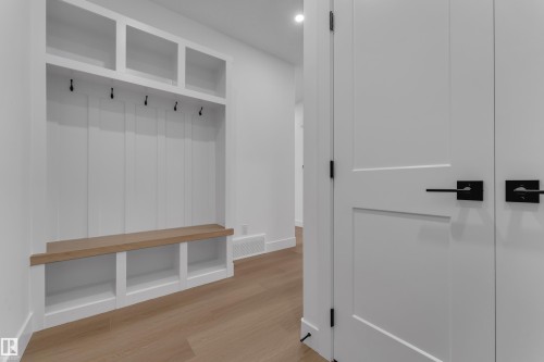Built-in mudroom storage featuring a wood-finish bench with cubbies, upper open shelving, and wall hooks - 794 Bank Drive, Leduc, AB 