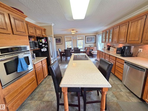 Kitchen featuring wood cabinetry, stainless steel appliances, a long center island with seating, ceramic tile flooring & quartz countertops - 9131 Township Road 554, Rural St. Paul County, AB 