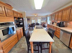 Kitchen featuring wood cabinetry, stainless steel appliances, a long center island with seating, ceramic tile flooring & quartz countertops - 
