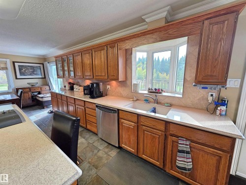 Kitchen featuring wood cabinetry, light-toned countertops, a stainless steel dishwasher, a bay window, and tile flooring - 9131 Township Road 554, Rural St. Paul County, AB 