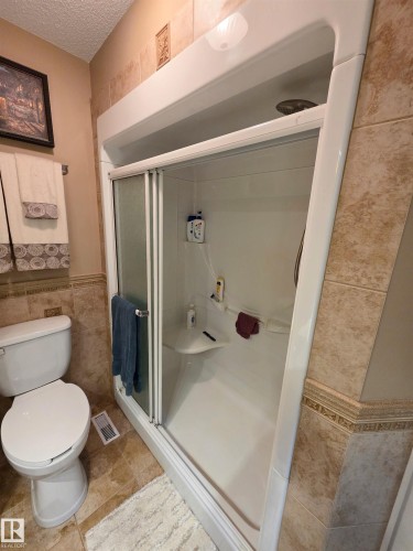 Spa-inspired bathroom featuring a sliding glass shower enclosure with chrome hardware, ceramic tile surround, and a ceramic pedestal sink - 9131 Township Road 554, Rural St. Paul County, AB 