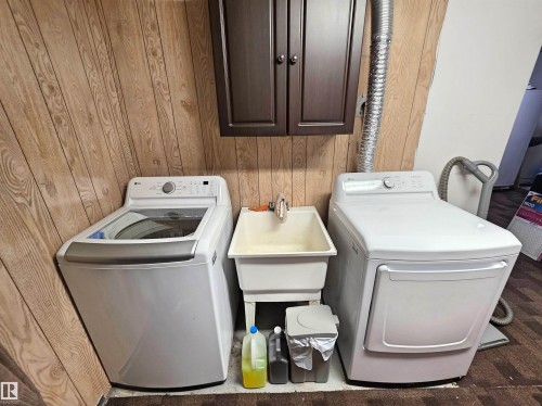 Wood-finish wall paneling, built-in wall cabinetry, utility sink, and installed washer and dryer units - 9131 Township Road 554, Rural St. Paul County, AB 