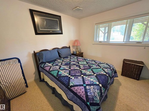 Bedroom featuring a window with horizontal blinds, neutral carpet flooring, and a textured ceiling - 9131 Township Road 554, Rural St. Paul County, AB 