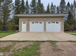 Two-car garage with overhead doors featuring arched windows, exterior lighting fixtures, and tan siding - 