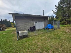 Chain-link fenced area with a white roll-up garage door, horizontal siding, and a sloped roofline - 