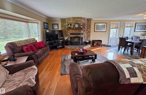 Stone-clad fireplace with wood-burning stove, hardwood flooring, bay window, and crown molding - 9131 Township Road 554, Rural St. Paul County, AB 