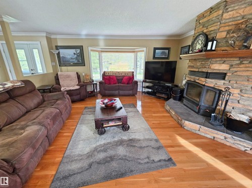 Wood-finish flooring throughout, a stone-faced fireplace with a hearth, a bay window with blinds, and white trim molding - 9131 Township Road 554, Rural St. Paul County, AB 